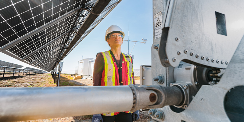 A woman in Personal Protective Equipment looking at a Solar Facility Equipment